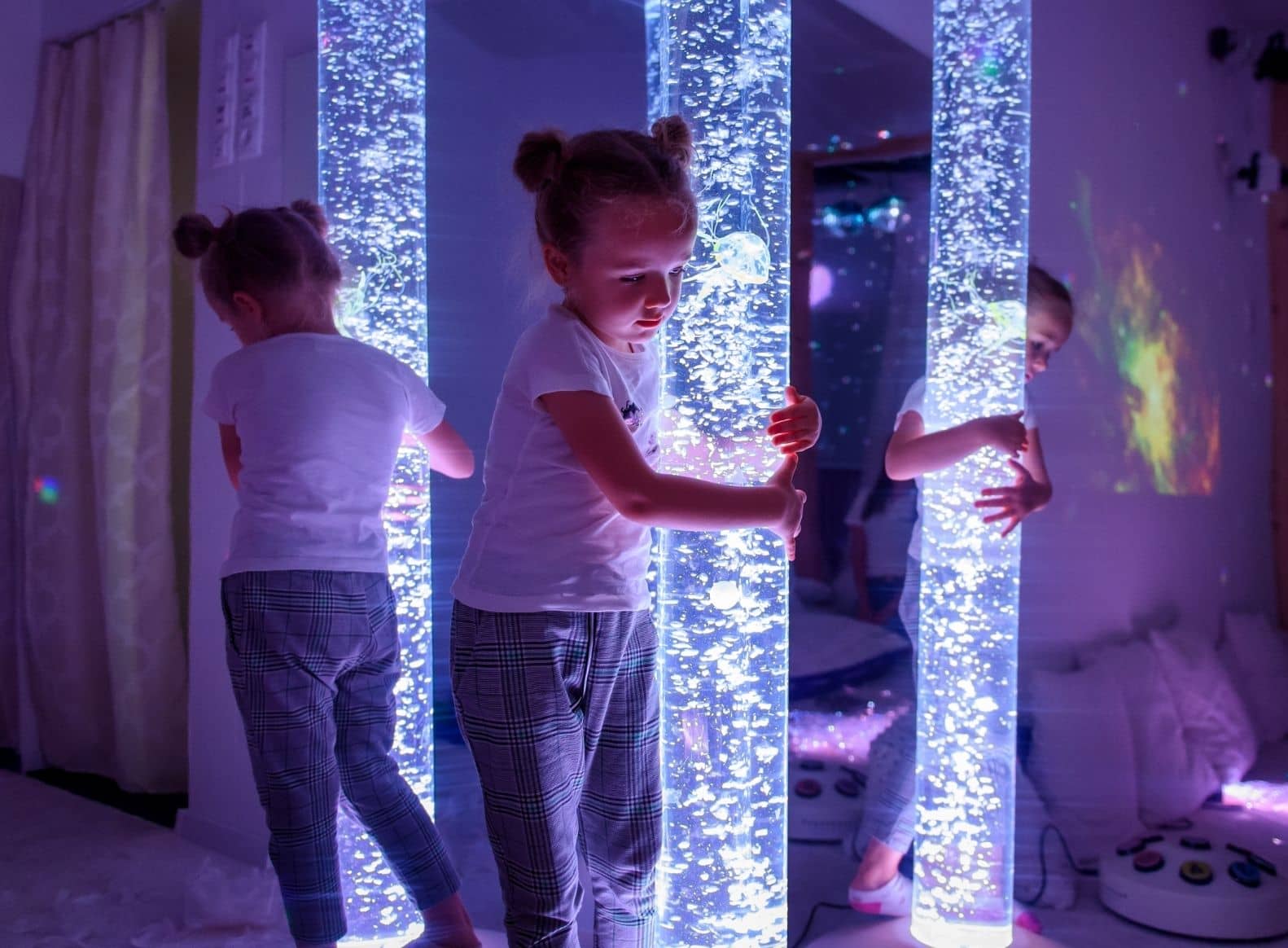 girl standing at bubble tube in front of mirror sensory room